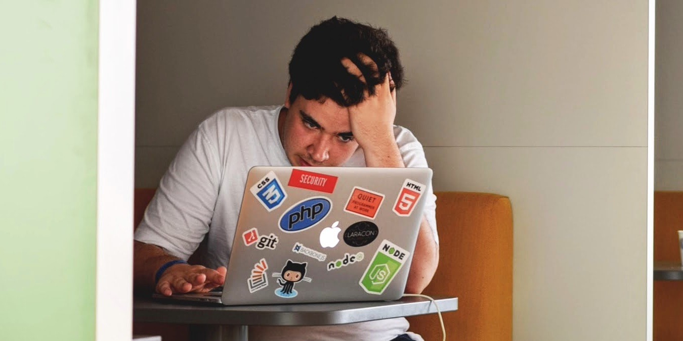 Photo of a person using their Mac with hand on head